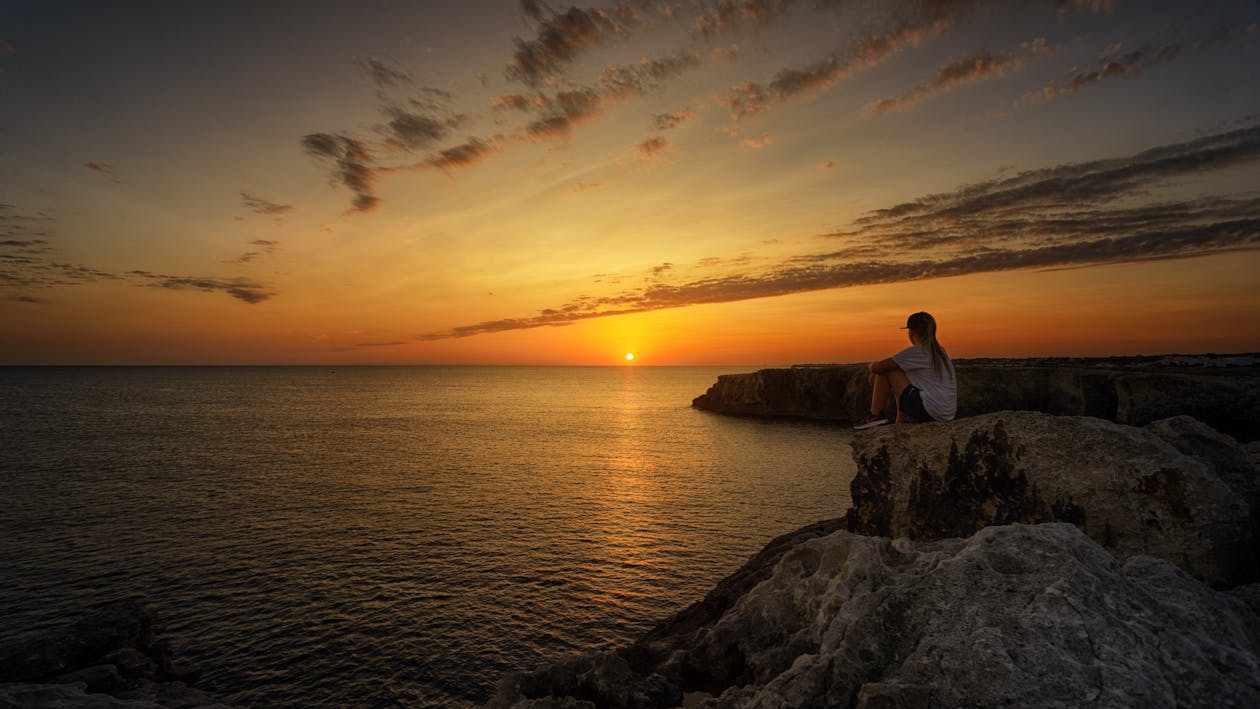 在日落期間坐在岩石上的人的照片