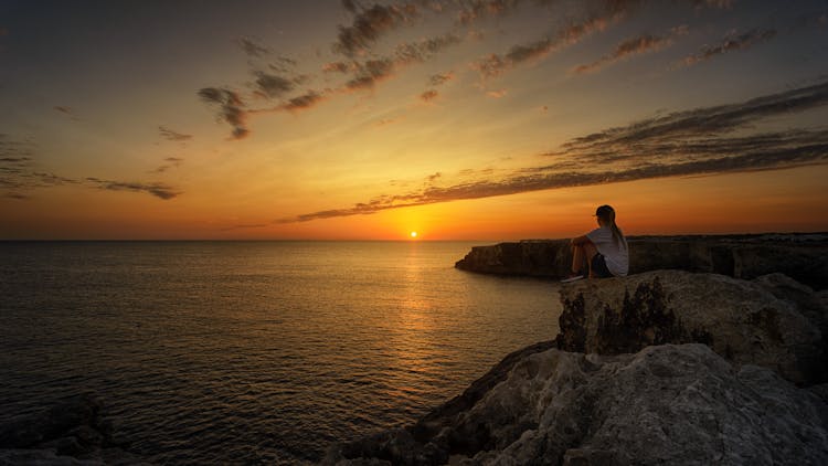 Photo Of Person Sitting On Rock During Sunset