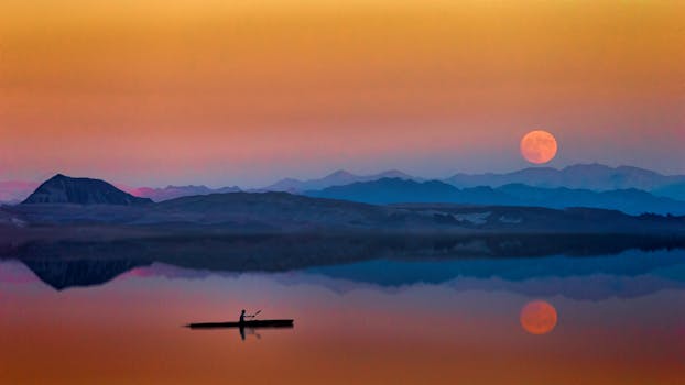 Serene kayak journey on reflective water with stunning sunset and moonrise over mountainous landscape.