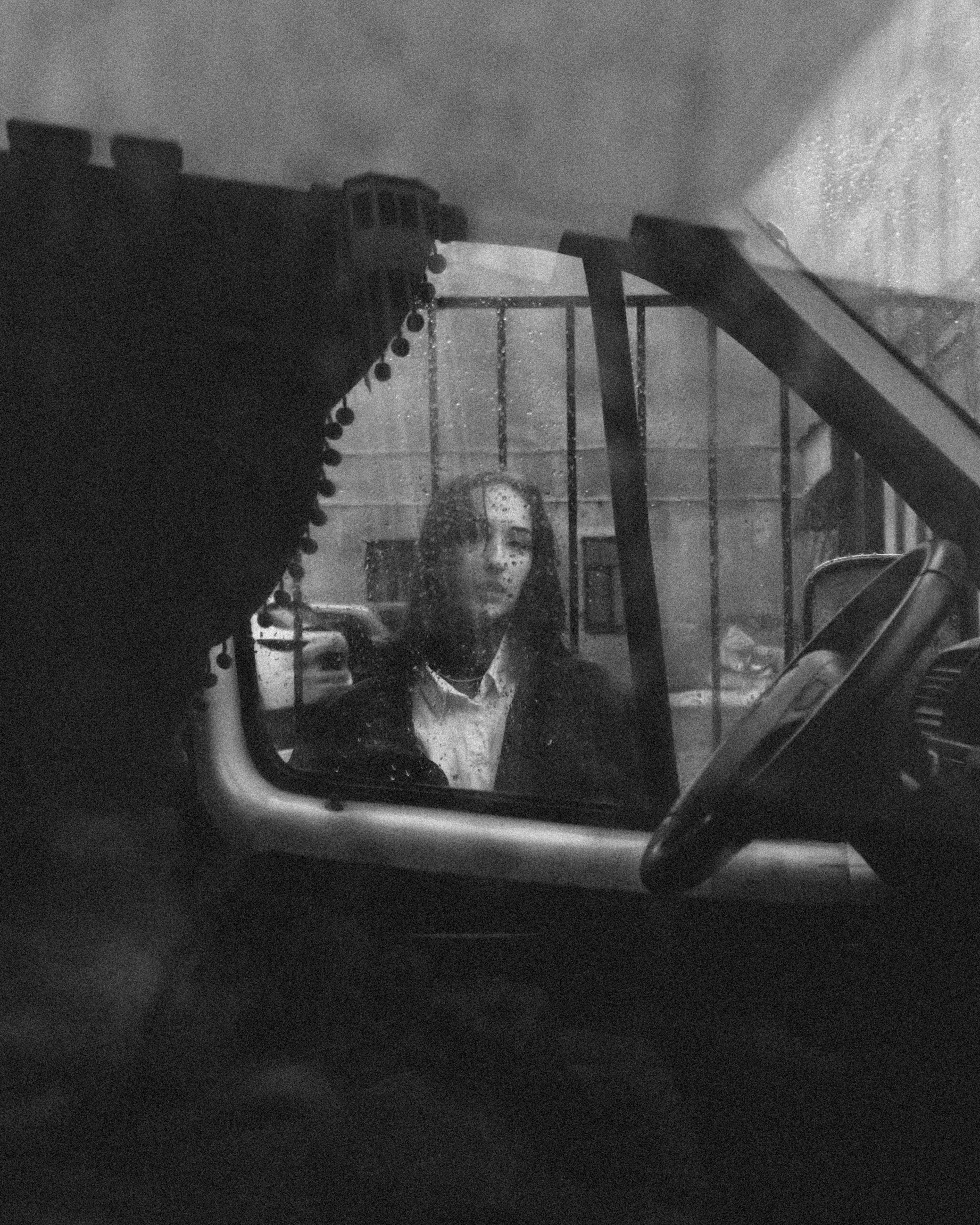 Black and white image capturing a woman's reflection through a rainy car window in Saint Petersburg.