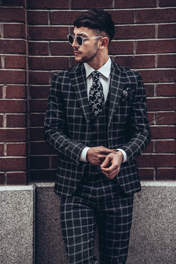 Stylish Man In Plaid Suit Leaning Against A Brick Wall