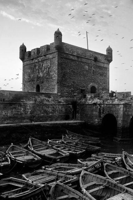 Black and white photo of the historic Scala fortress overlooking the wooden boats at Essaouira's port in Morocco.