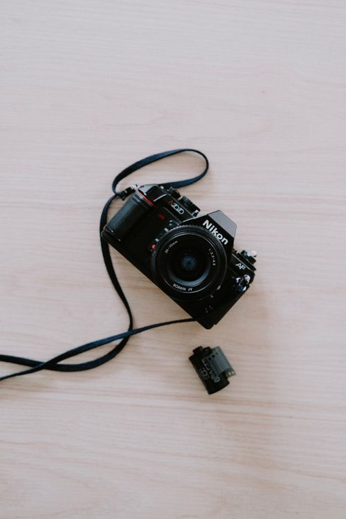 Free Classic film camera placed diagonally on a light wooden surface with lens and strap visible. Stock Photo