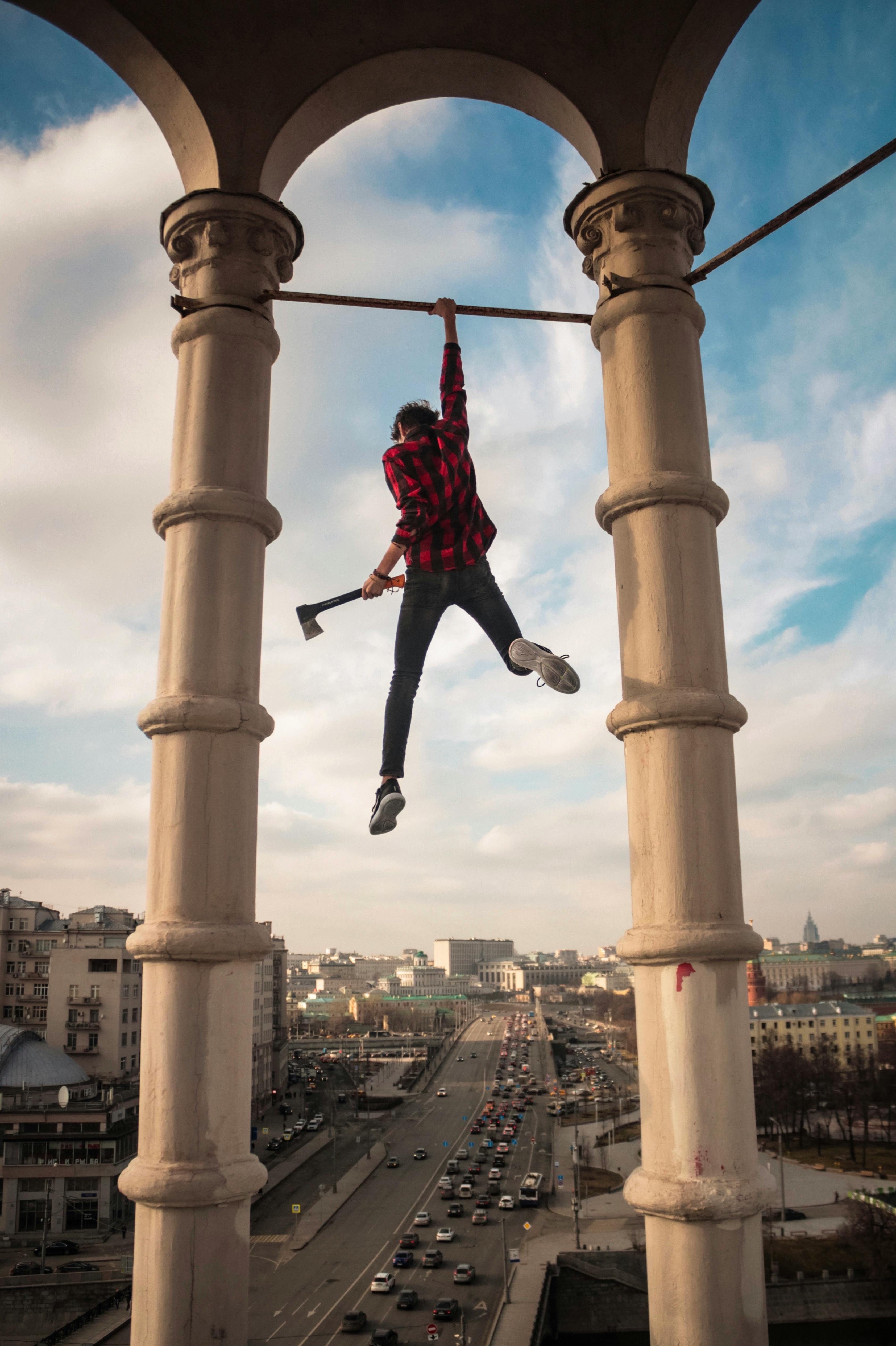 Person hanging from building in Moscow, holding an axe with cityscape in background.