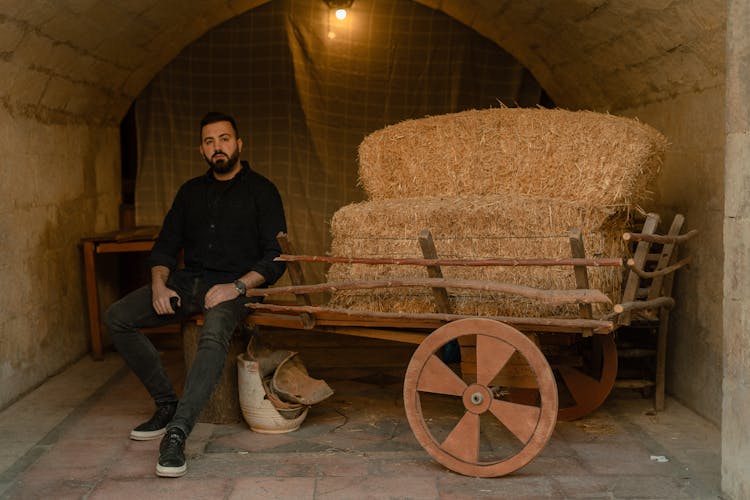 Man Sitting On A Vintage Cart With Hale Bale On It 