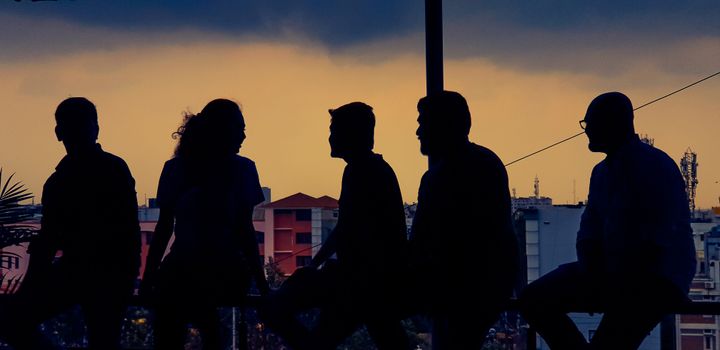 Silhouette of diverse group chatting against Bengaluru skyline at twilight.