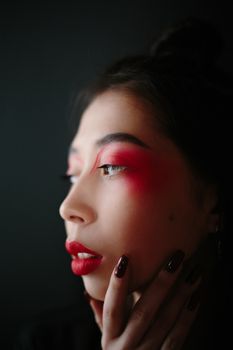 A striking side view of a woman with vivid red makeup in a studio setting.