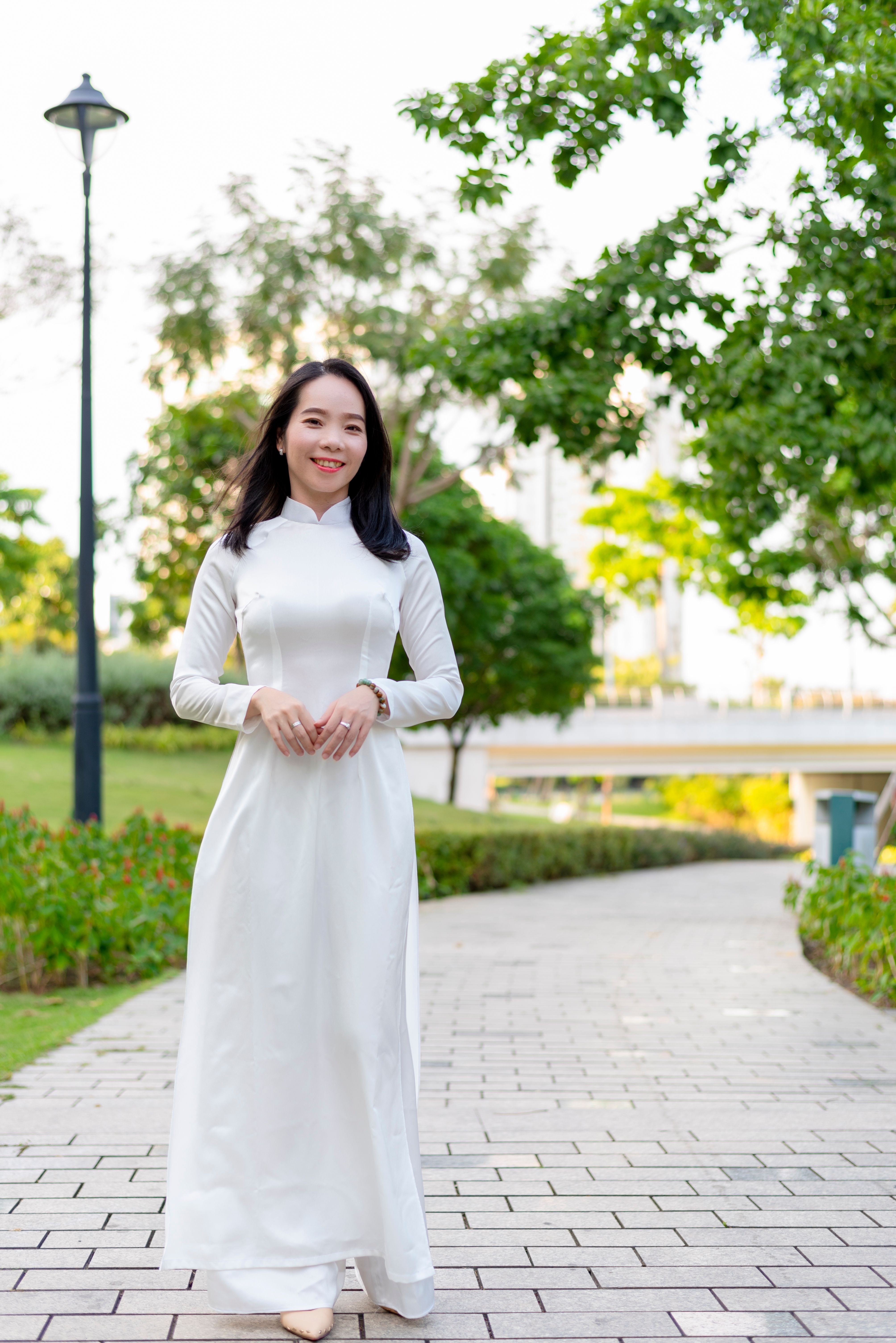 Asian woman in traditional white dress smiling and walking outdoors in a park, Ho Chi Minh City.