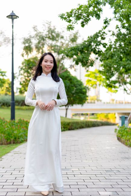 Asian woman in traditional white dress smiling and walking outdoors in a park, Ho Chi Minh City.