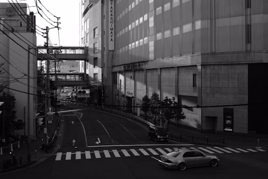 A deserted city street in black and white with buildings and parked cars.
