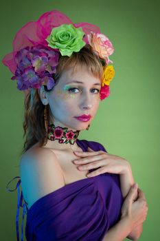 Portrait of a fashionable woman with floral headband and glitter makeup on a green background.