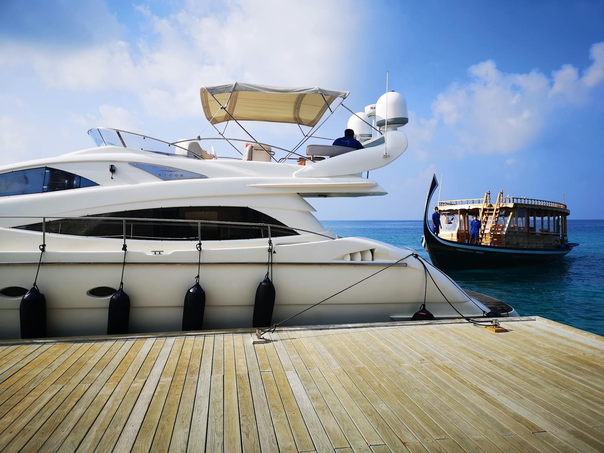 A picturesque scene of a luxury yacht and traditional boats docked in the Maldives, under a bright blue sky.