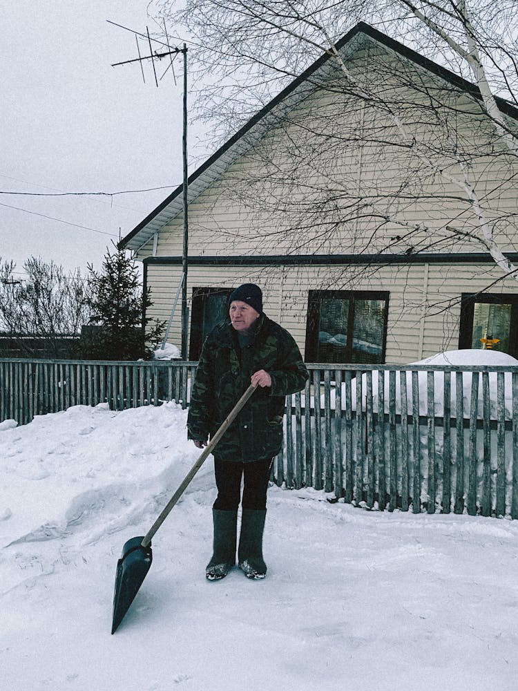 Elderly Man In Winter Coat Holding A Snow Shovel