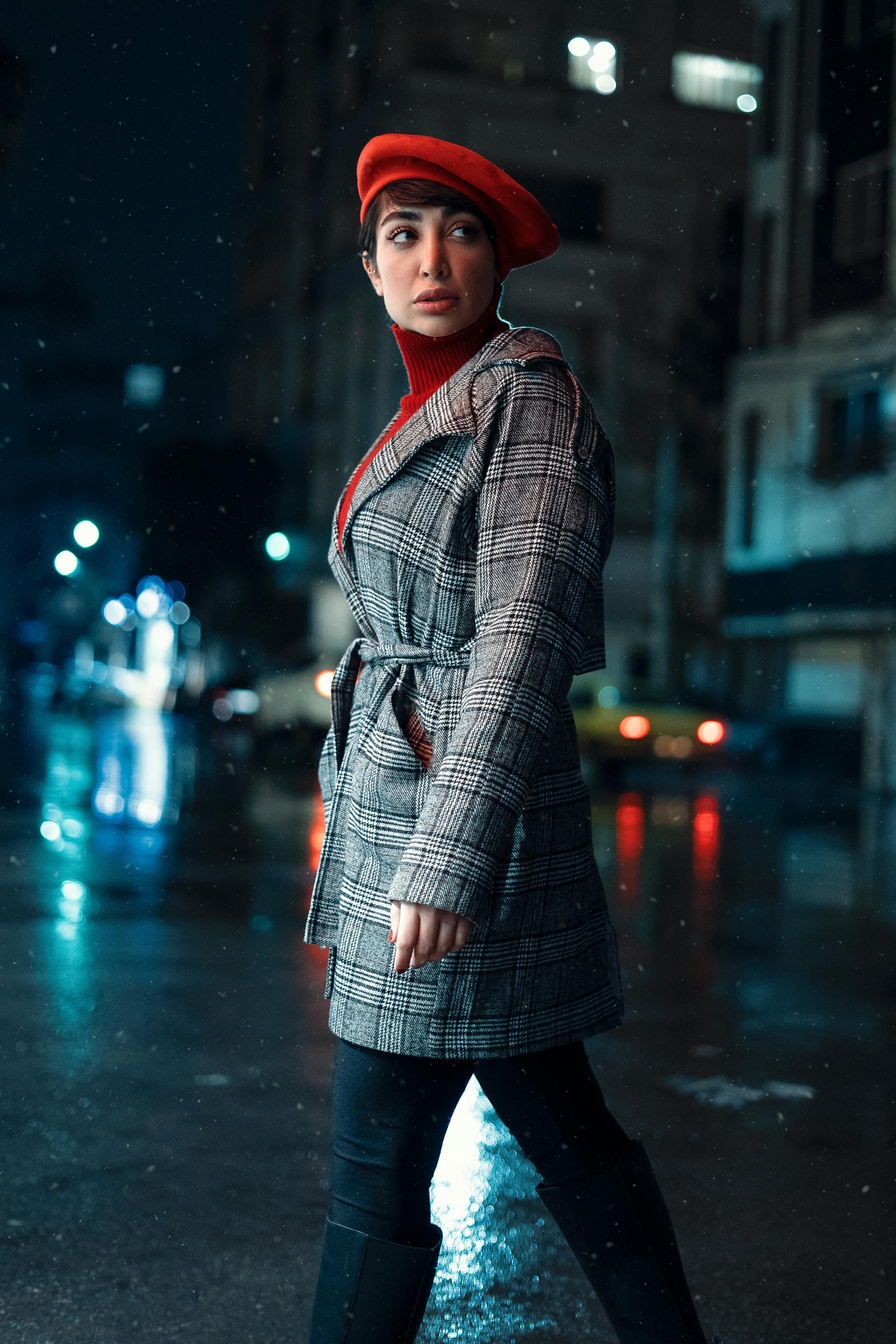 Woman in a chic coat and beret walking on a rainy Paris night street with city lights.
