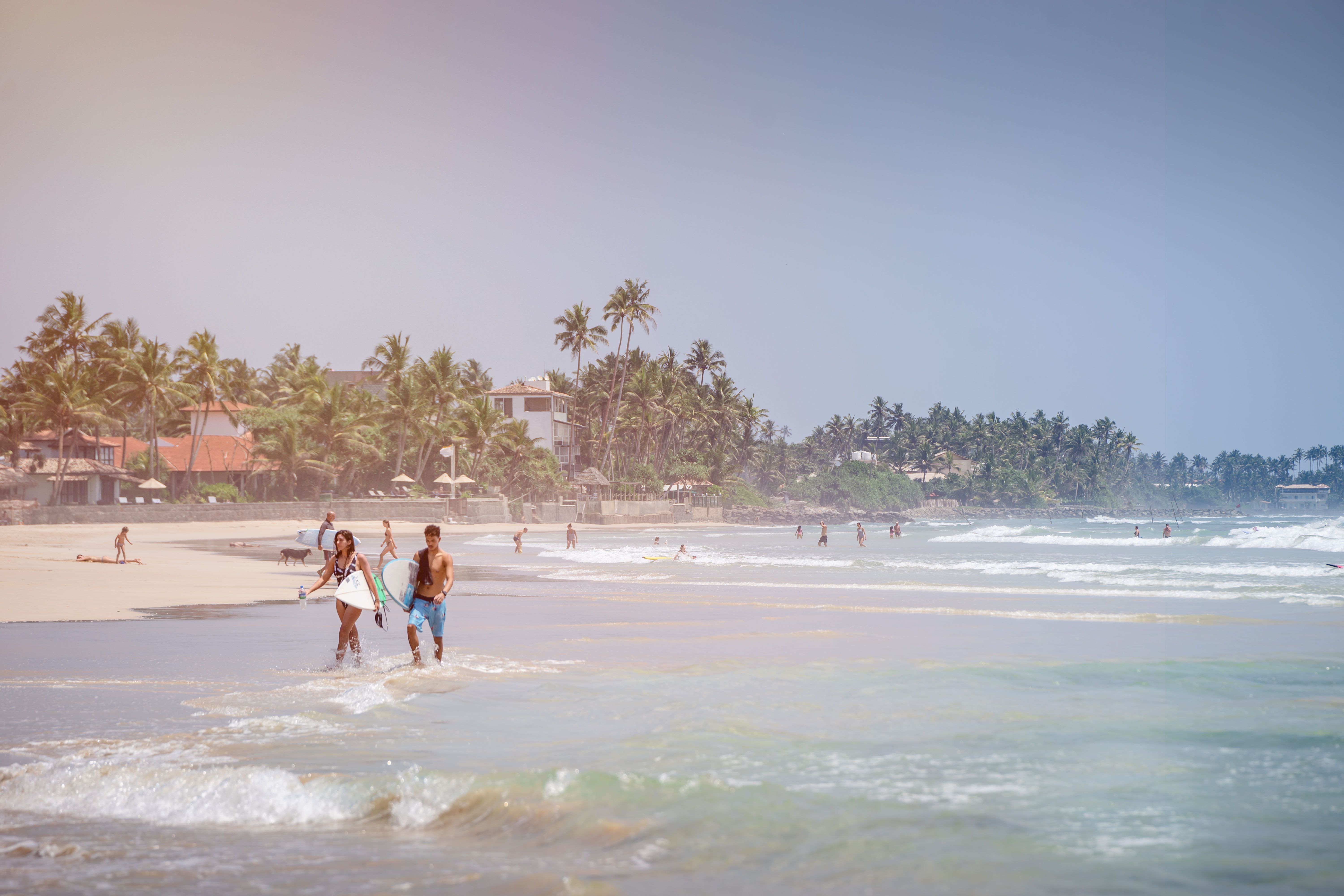 Surfers carrying their boards along the beach in Sri Lanka