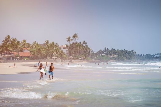Couple carrying surfboards along the sunny beach in Dambulla, Sri Lanka.