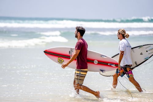 Free Two surfers carrying boards on a sunny day at Dambulla Beach, Sri Lanka. Stock Photo