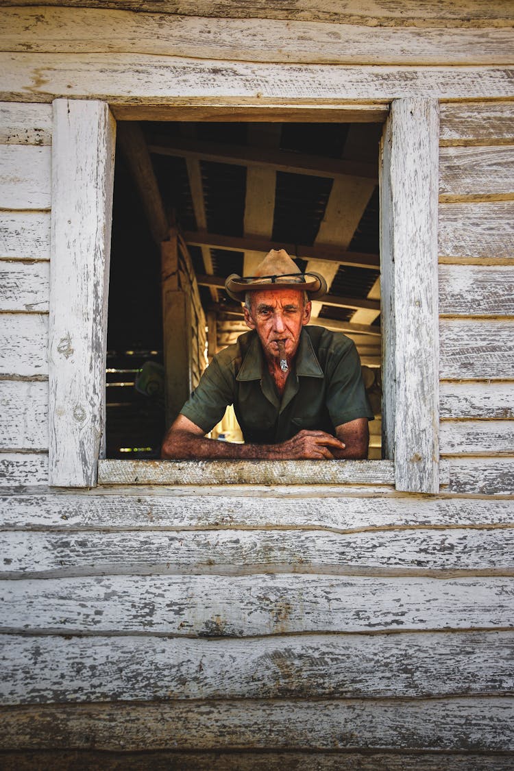 Old Man Looking From Window In Wooden Cabin