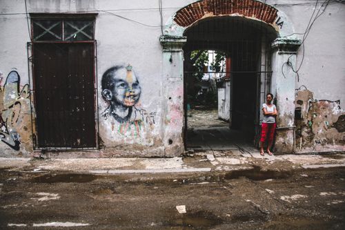 Free A woman standing by a graffitied wall in a decaying urban street setting. Stock Photo