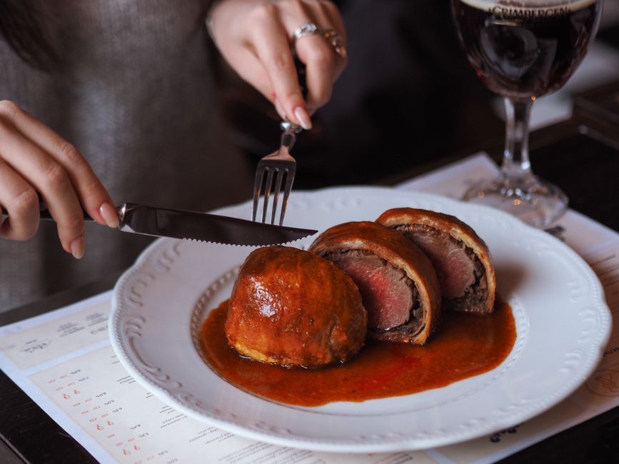 Sliced beef wellington with rich sauce on white plate`