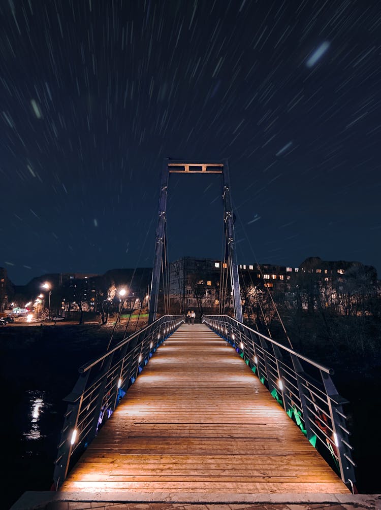 A Couple Walking On A Brown Wooden Bridge During Night Time