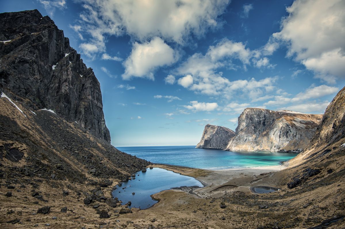 Turquoise water and white sand at a remote beach, framed by steep cliffs on both sides.