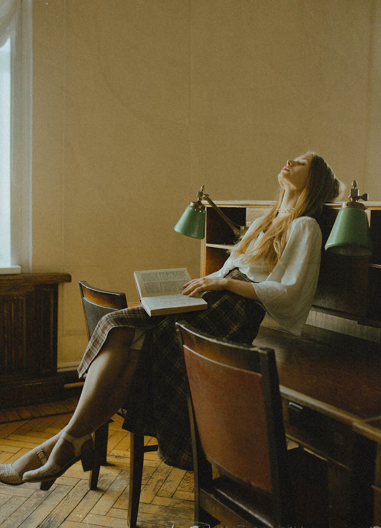 Woman Sitting On Desk Holding Book 