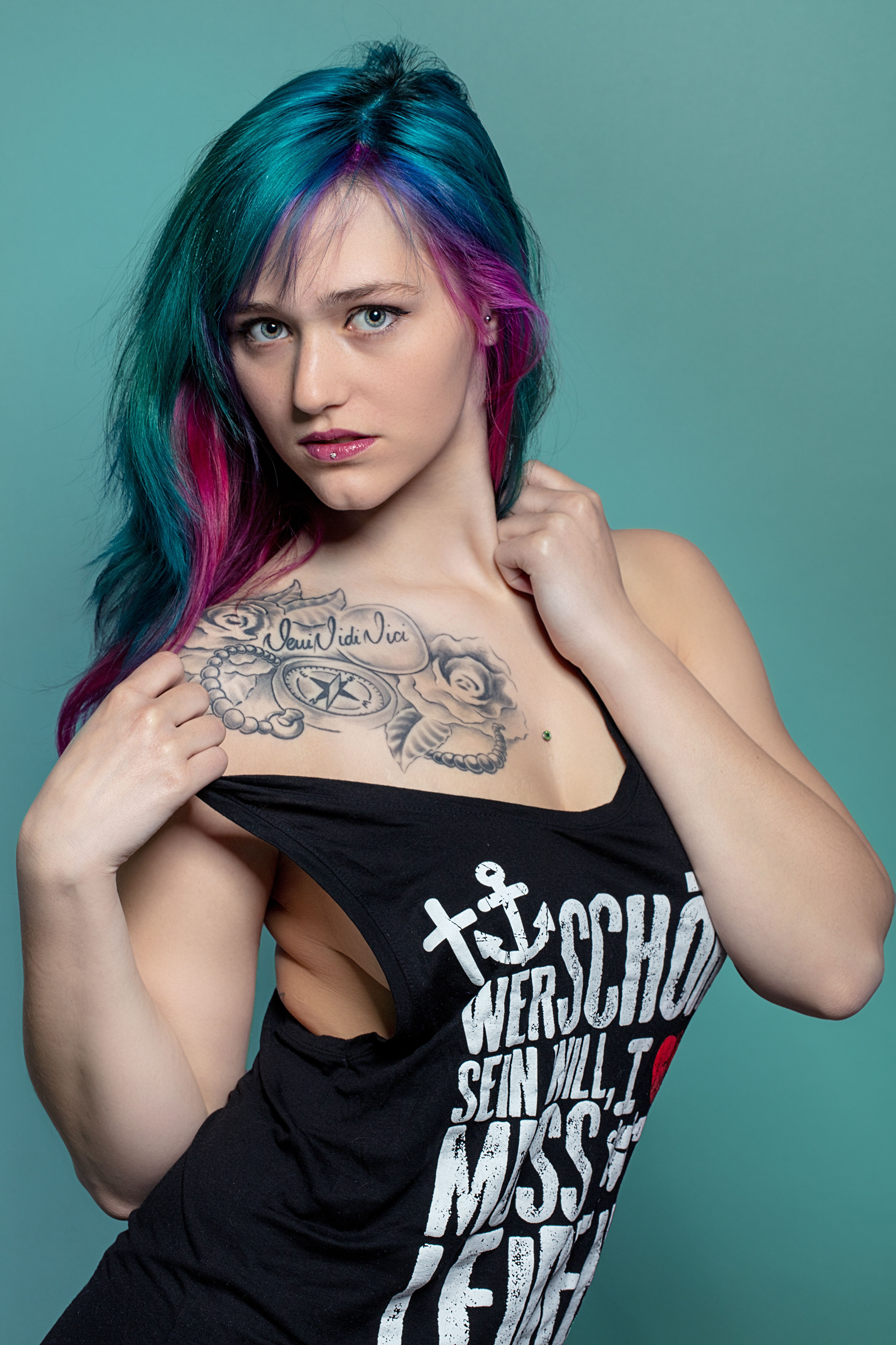 Portrait of a woman with vibrant colorful hair and tattoos posing confidently in a black top.