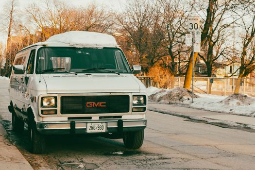 Vintage GMC van covered with snow parked on a snowy street intersection with winter trees around.