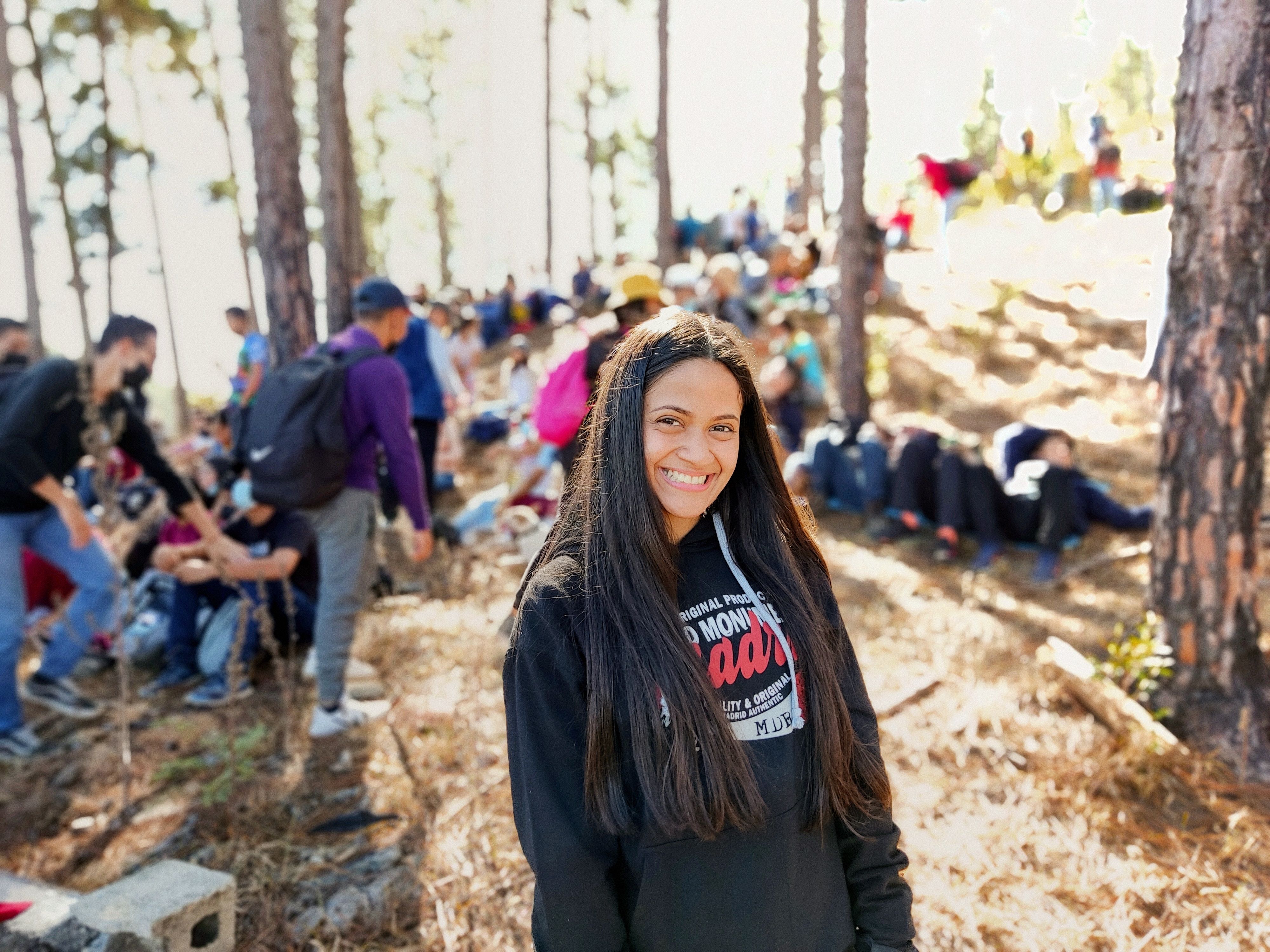 A cheerful woman standing in a forest with a group of people enjoying nature together.