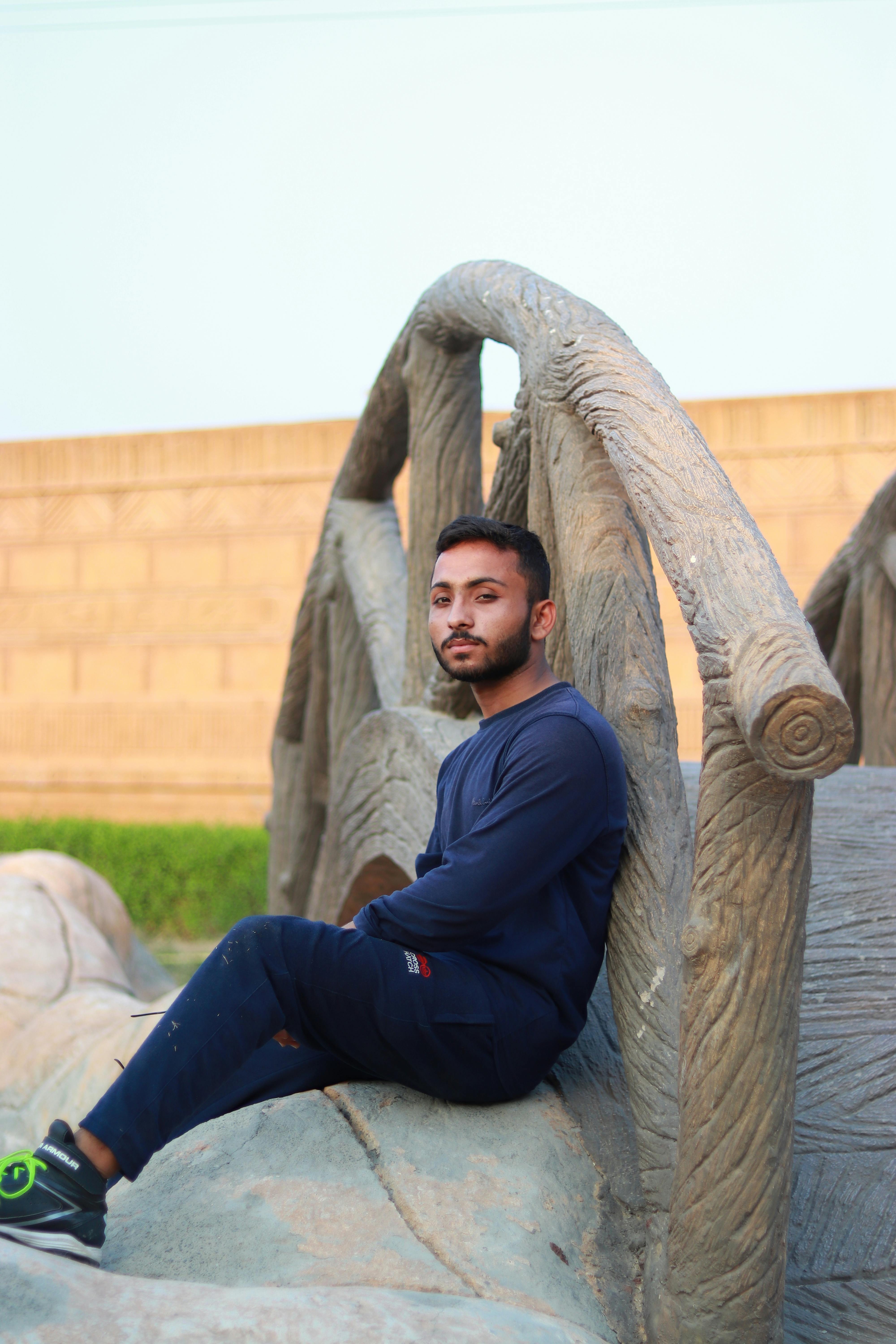 A young Asian man in casual attire leans against an artistic stone sculpture outdoors.