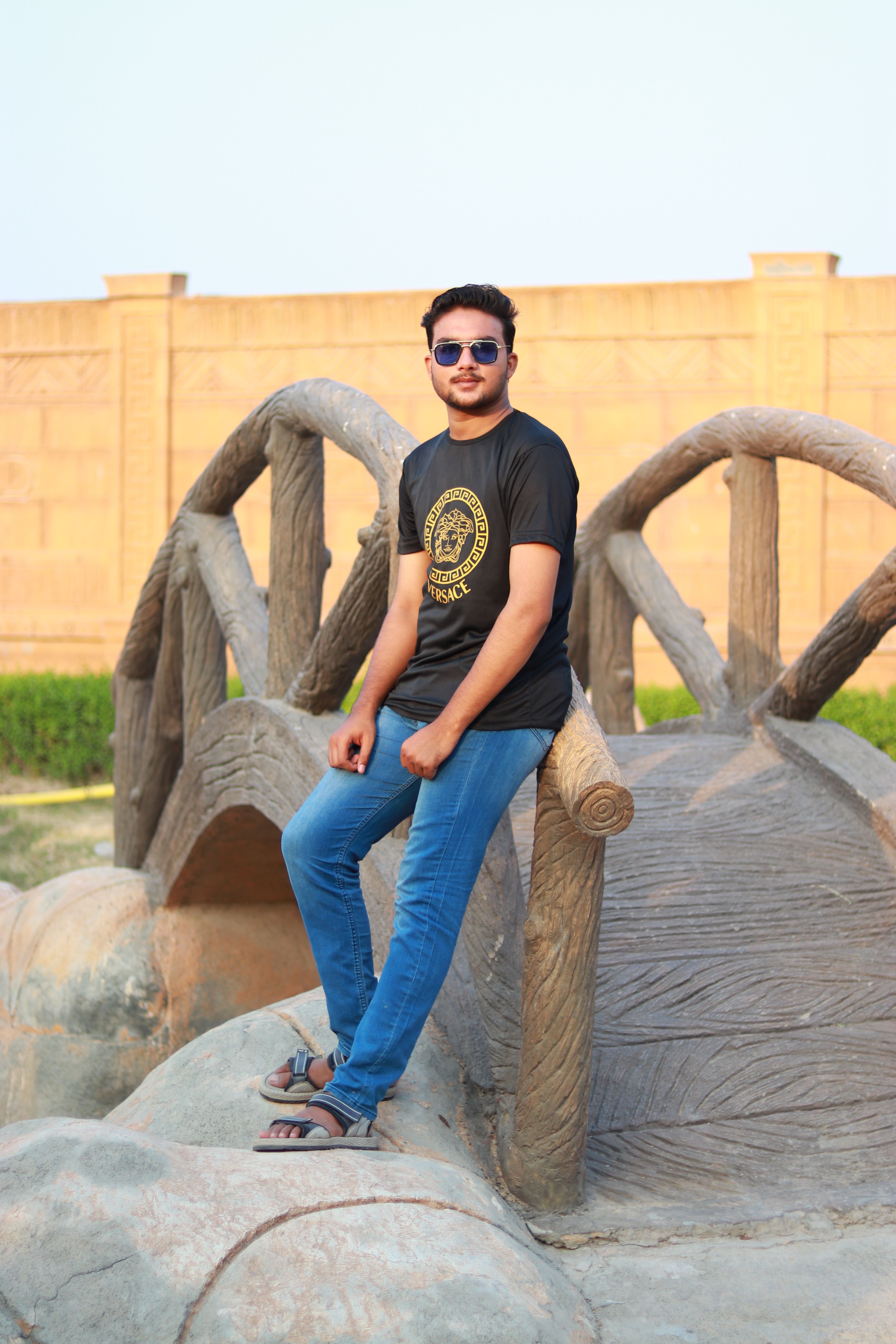 Portrait of a young man in casual attire sitting on a unique wooden bridge outdoors.