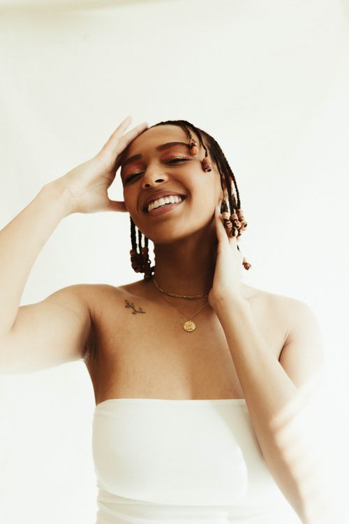 Free A joyful portrait of a woman with braided hair, smiling in a white outfit against a bright background. Stock Photo