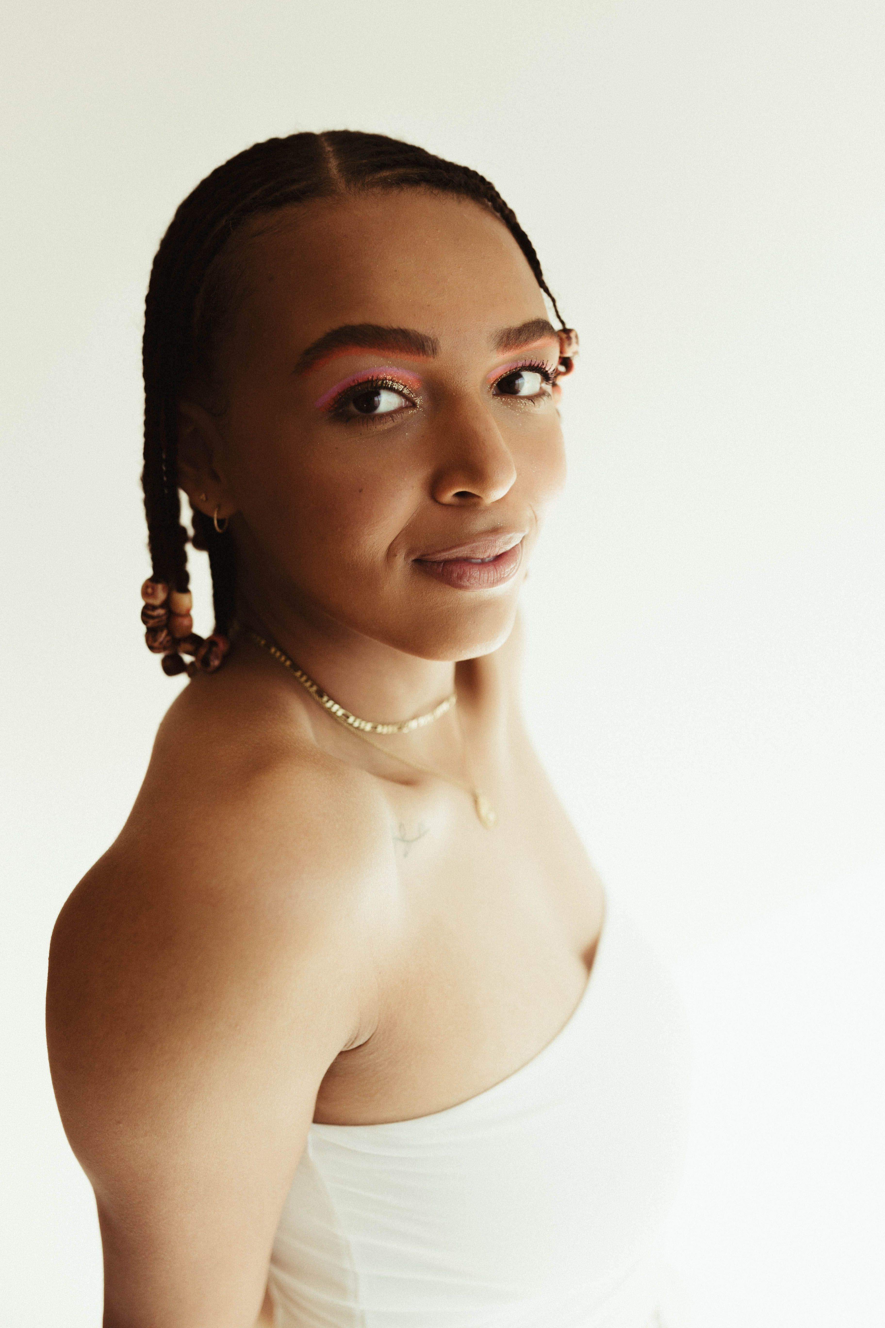 Stylish portrait of a woman with cornrows and vibrant eye makeup captured in a studio setting.