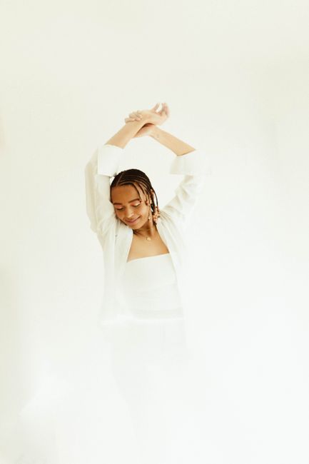 Elegant fashion portrait of a woman posing gracefully in a white outfit against a minimalist background.