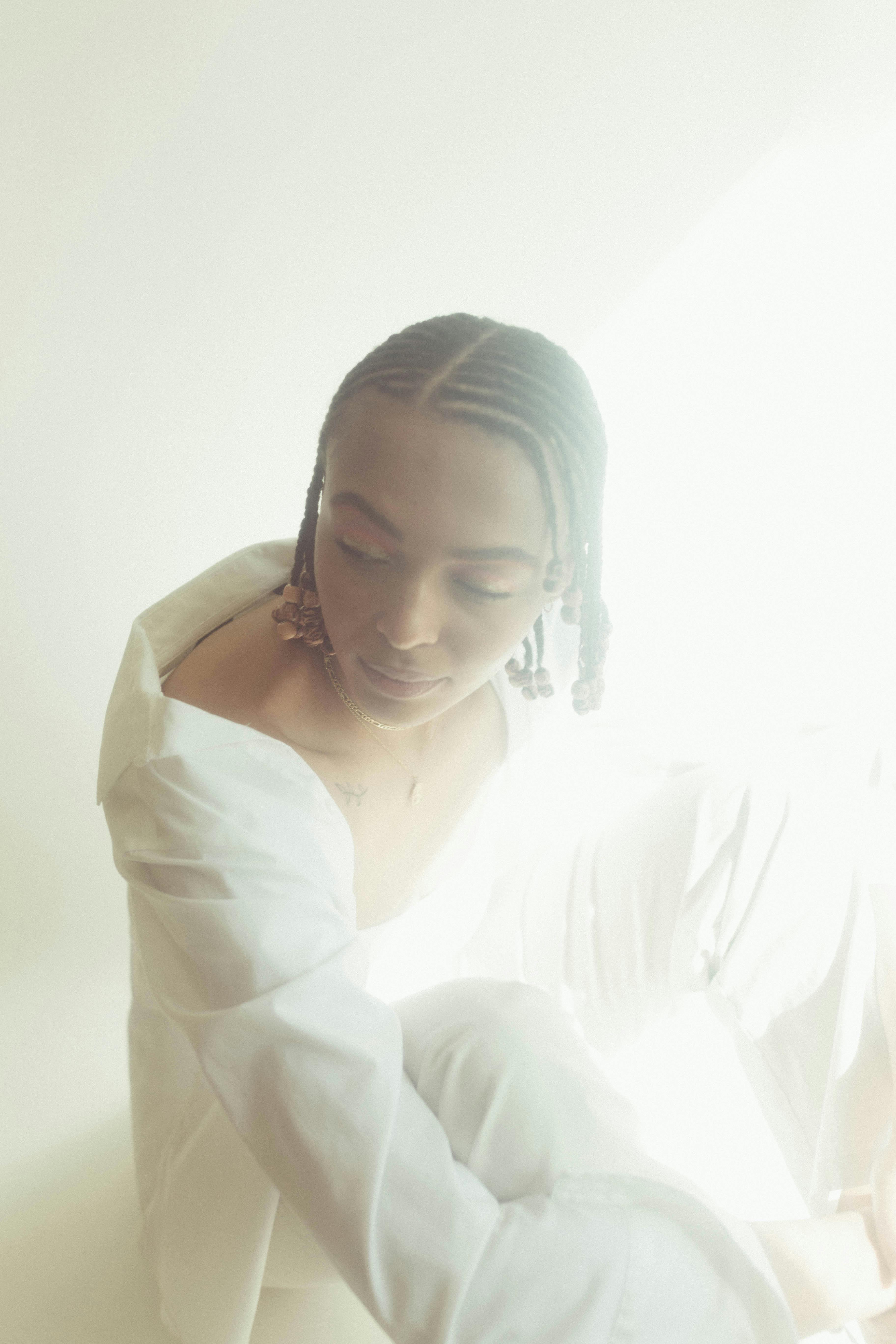 A serene studio portrait of a woman in a white outfit with braided hair and delicate lighting.