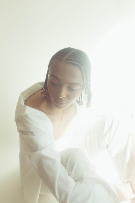 A serene studio portrait of a woman in a white outfit with braided hair and delicate lighting.