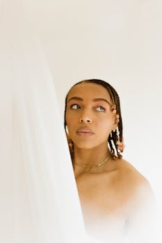Stunning portrait of a woman with cornrows and elegant makeup, looking contemplative against a white background.