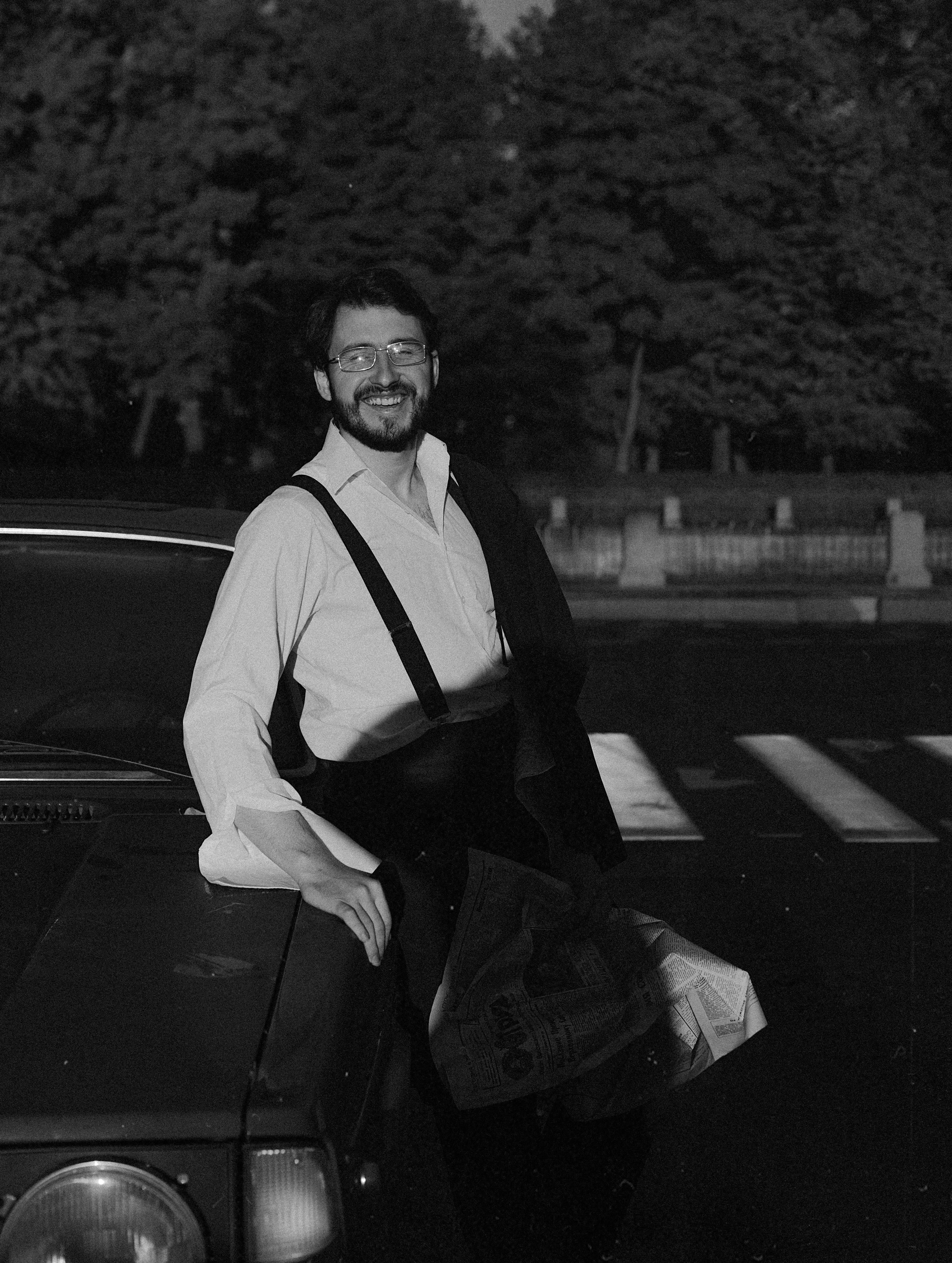 Smiling man with facial hair leaning on a car holding a newspaper in Saint Petersburg, Russia.