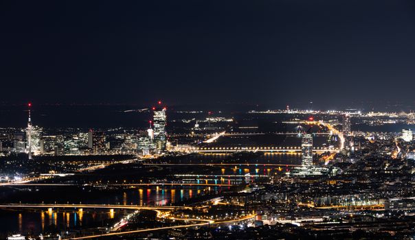Stunning nighttime view of Vienna, Austria with illuminated cityscape and Danube River reflections.