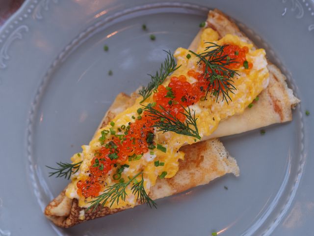 Scrumptious pancake topped with caviar, scrambled eggs, and fresh herbs on a decorative plate.
