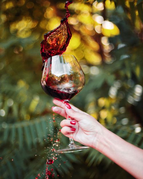 Free Close-up of a hand holding a glass of red wine splashing outdoors. Stock Photo