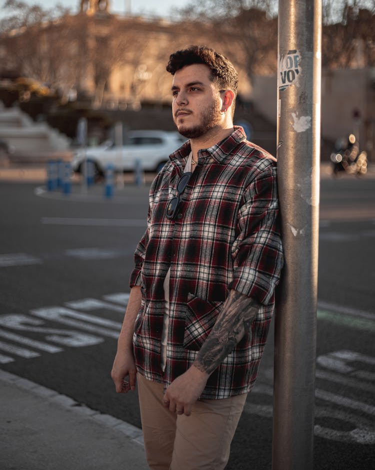 Man Wearing A Plaid Shirt Leaning On A Metal Pole