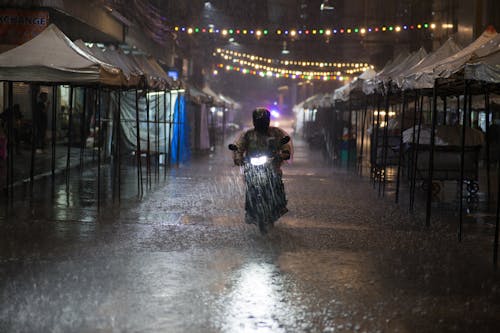 A Person Driving a Motorcycle on a Street while Raining