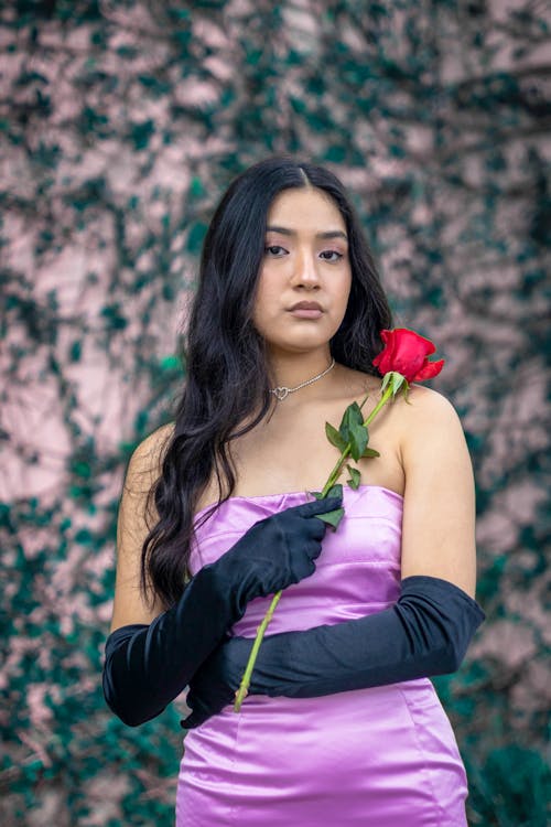 Woman in Purple Tube Dress Holding Red Rose while Looking at the Camera