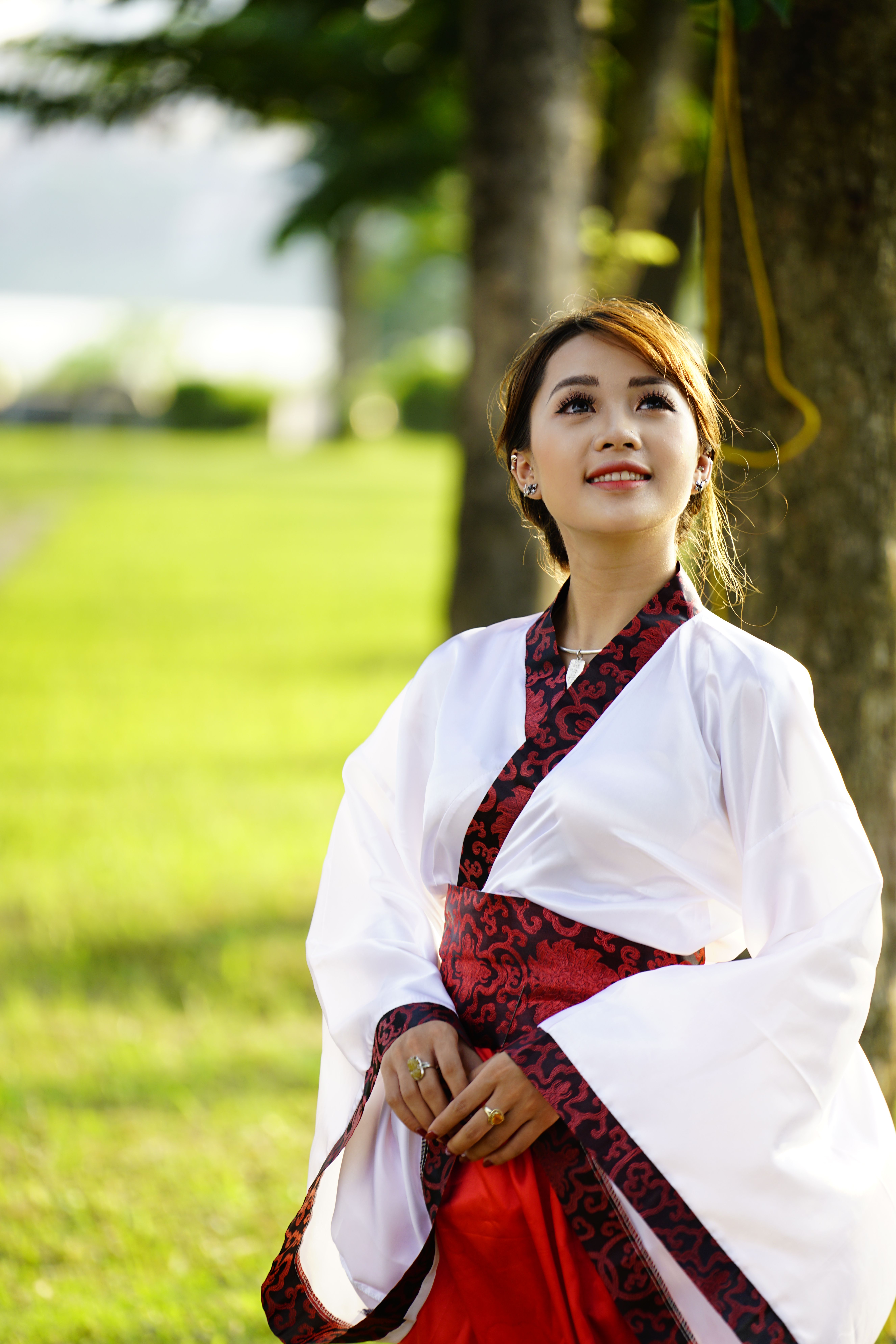 Woman in red and white kimono looking up in a sunny park.
