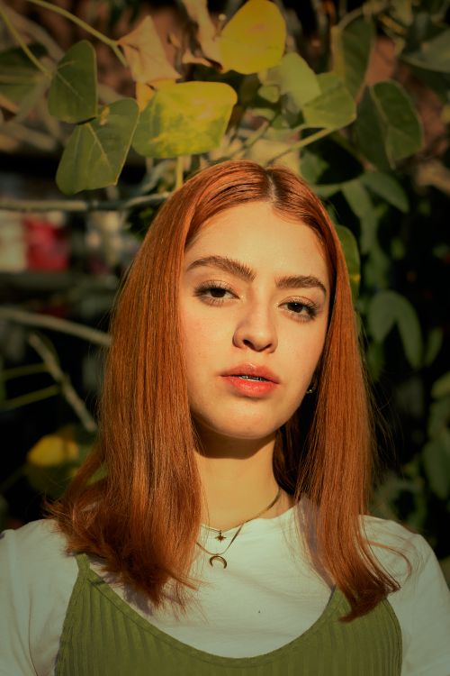Free Close-up portrait of a ginger-haired woman under sunlight with natural surroundings. Stock Photo