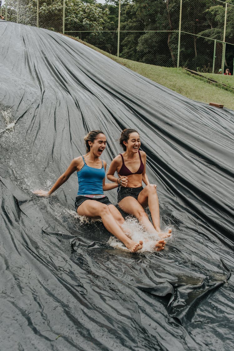 Young Women Holding Hands While Sliding Down A Slip N Slide