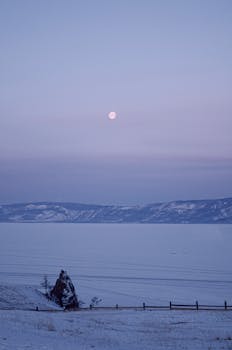 Captivating winter landscape featuring a full moon over snow-covered hills and a frozen lake.