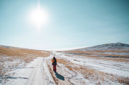 A solitary figure walks along a snow-covered path under a bright winter sun.